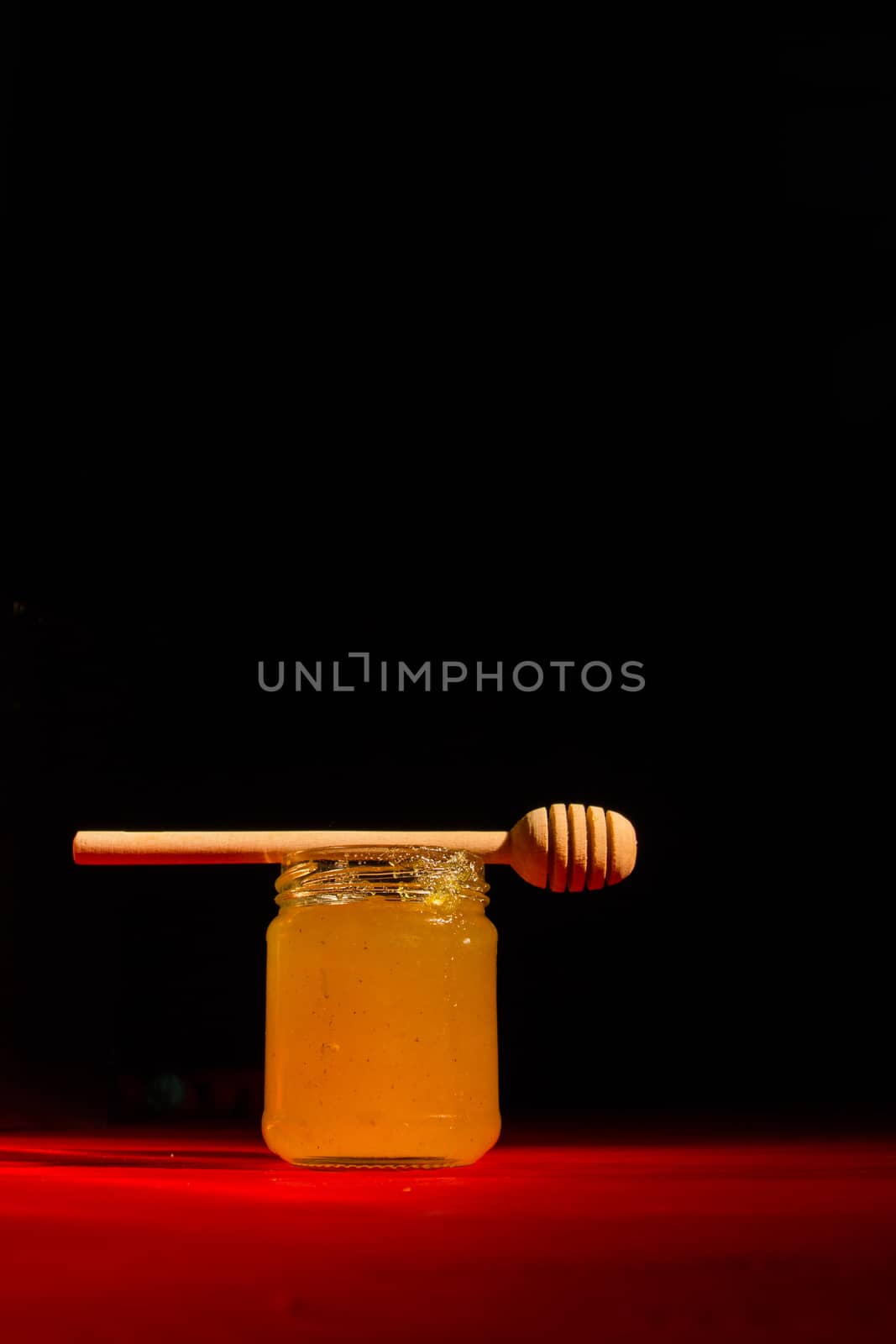 Honey with dipper on red wooden background with the the play of light and shadow