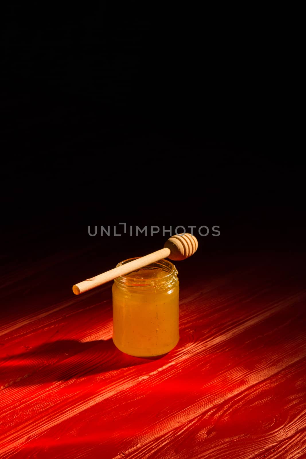 Honey with dipper on red wooden background with the the play of light and shadow