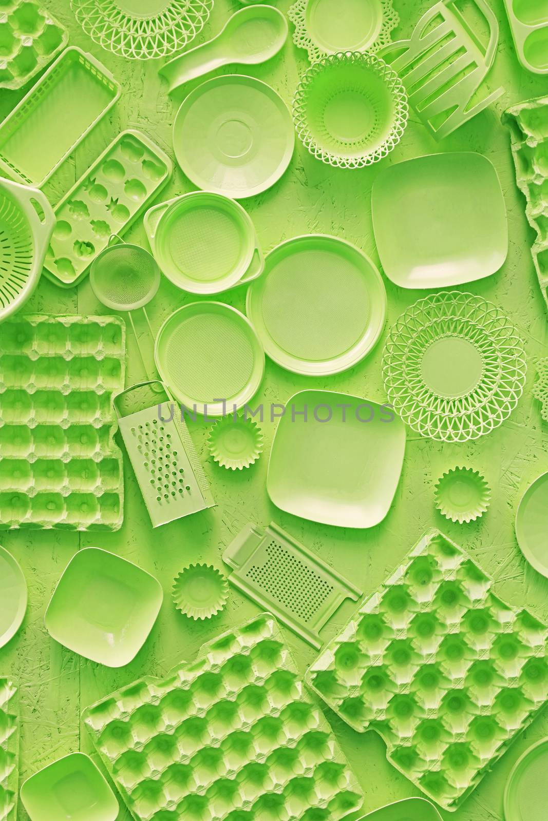 Close up flat lay of different green color painted kitchen utensils and tools, grater, spoon, egg carton, plastic disposable plates, elevated top view, directly above