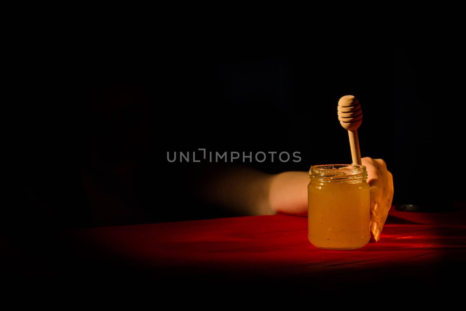 Honey with dipper on red wooden background with the the play of light and shadow