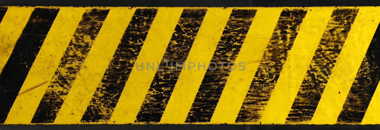 Old yellow weathered painted background with grunge black hazard sign stripes over dark