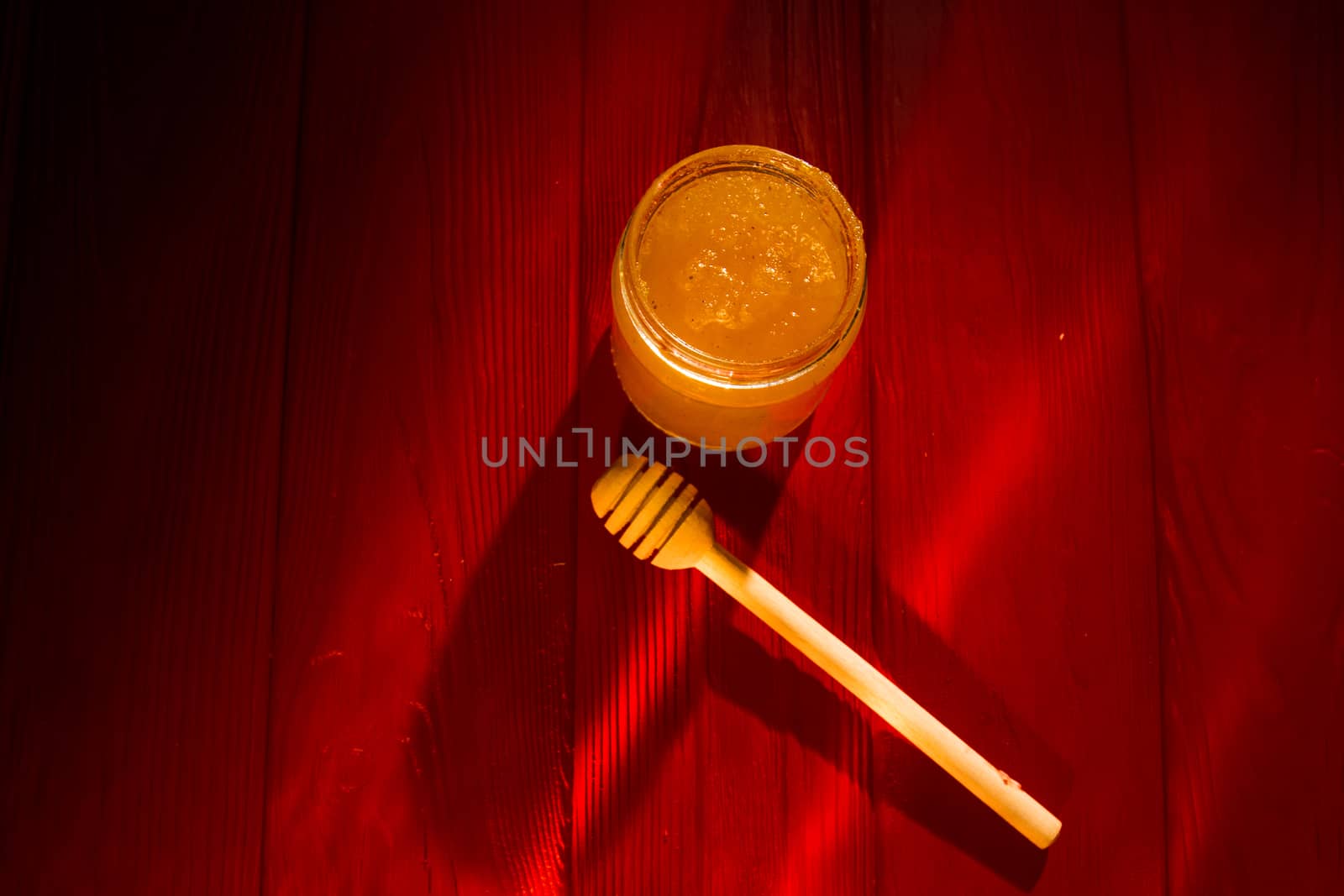 Honey with dipper on red wooden background with the the play of light and shadow