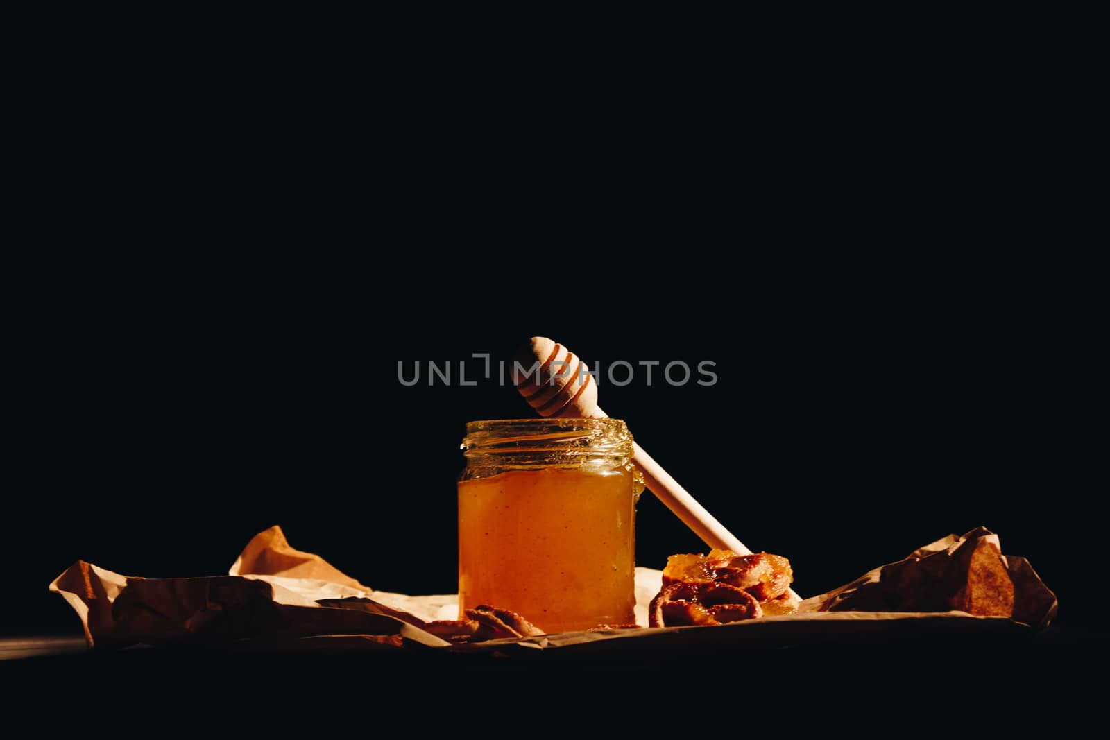 Honey with wooden honey dipper paper napkin and fruits on wooden table close up by yulaphotographer