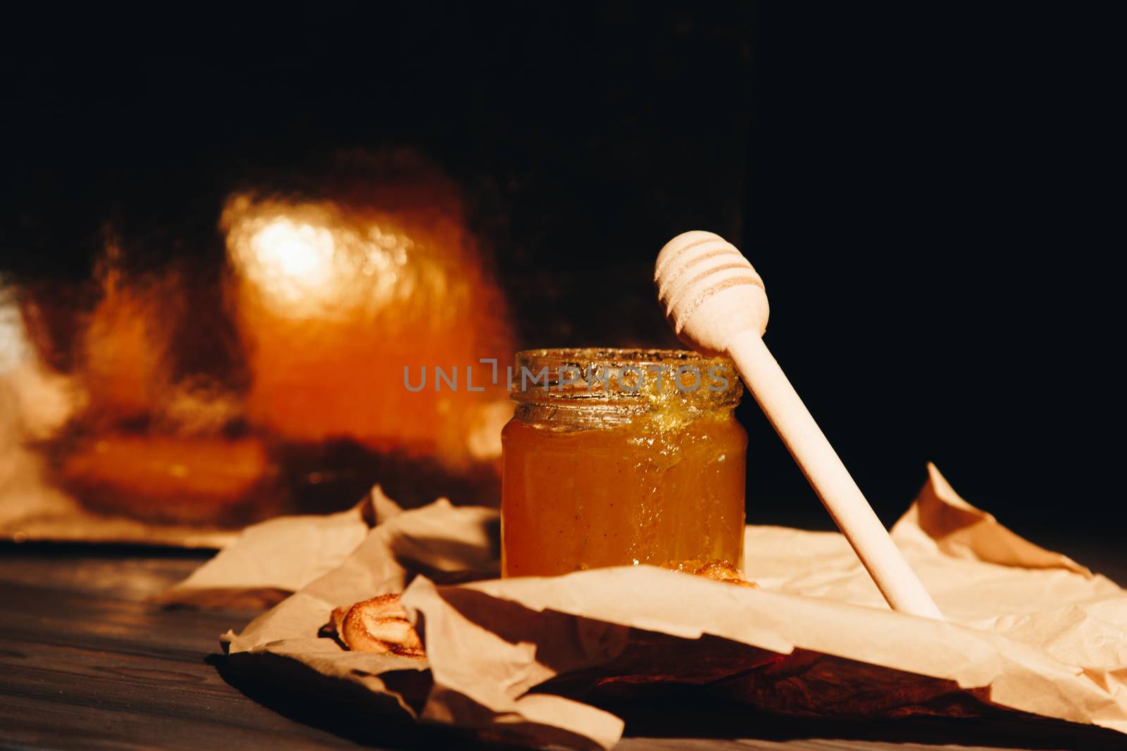 Honey with wooden honey dipper paper napkin and fruits on wooden table close up by yulaphotographer