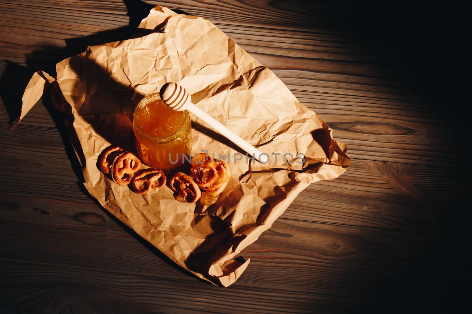 Honey with wooden honey dipper paper napkin and fruits on wooden table close up by yulaphotographer