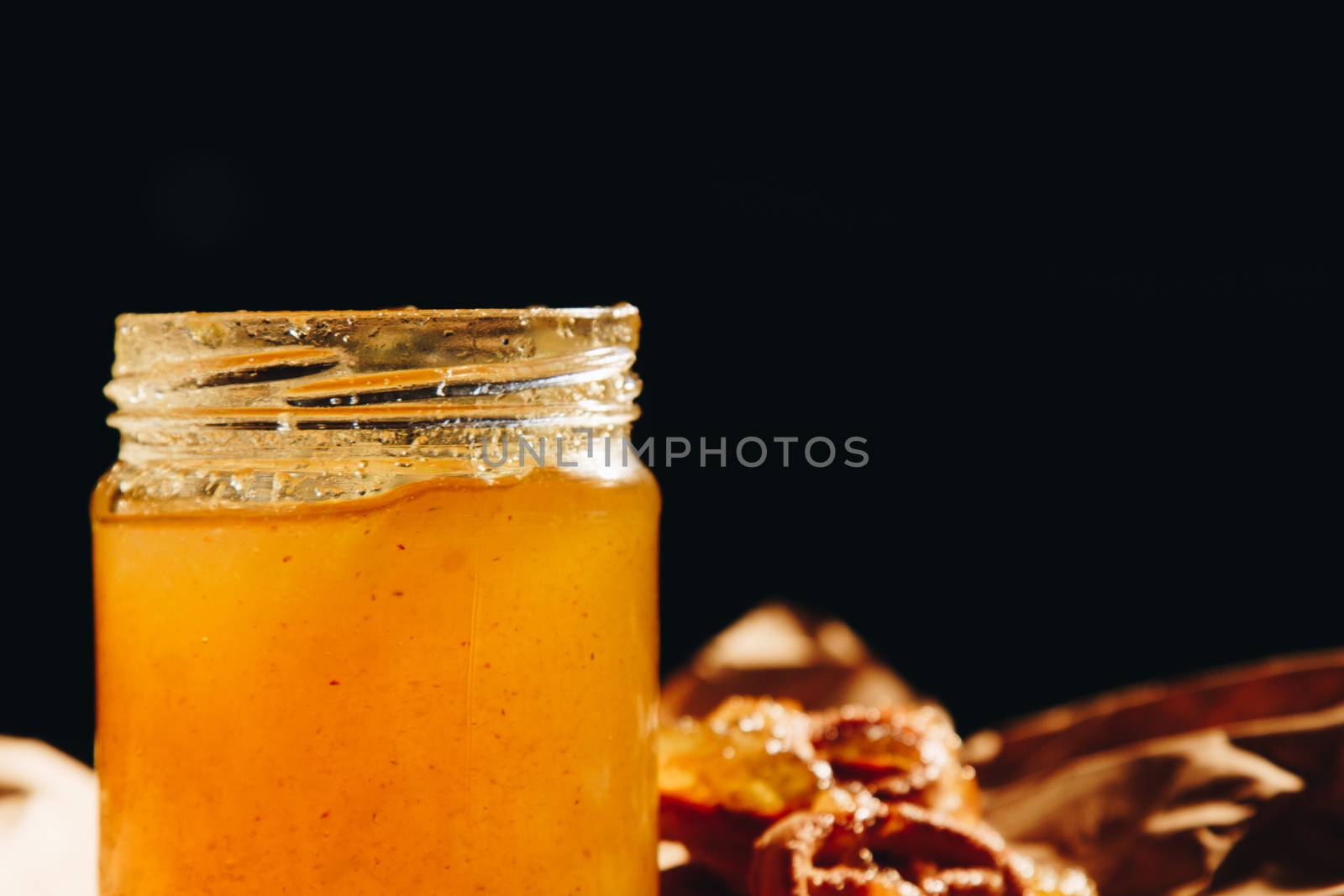 Honey with wooden honey dipper paper napkin and fruits on wooden table close up by yulaphotographer