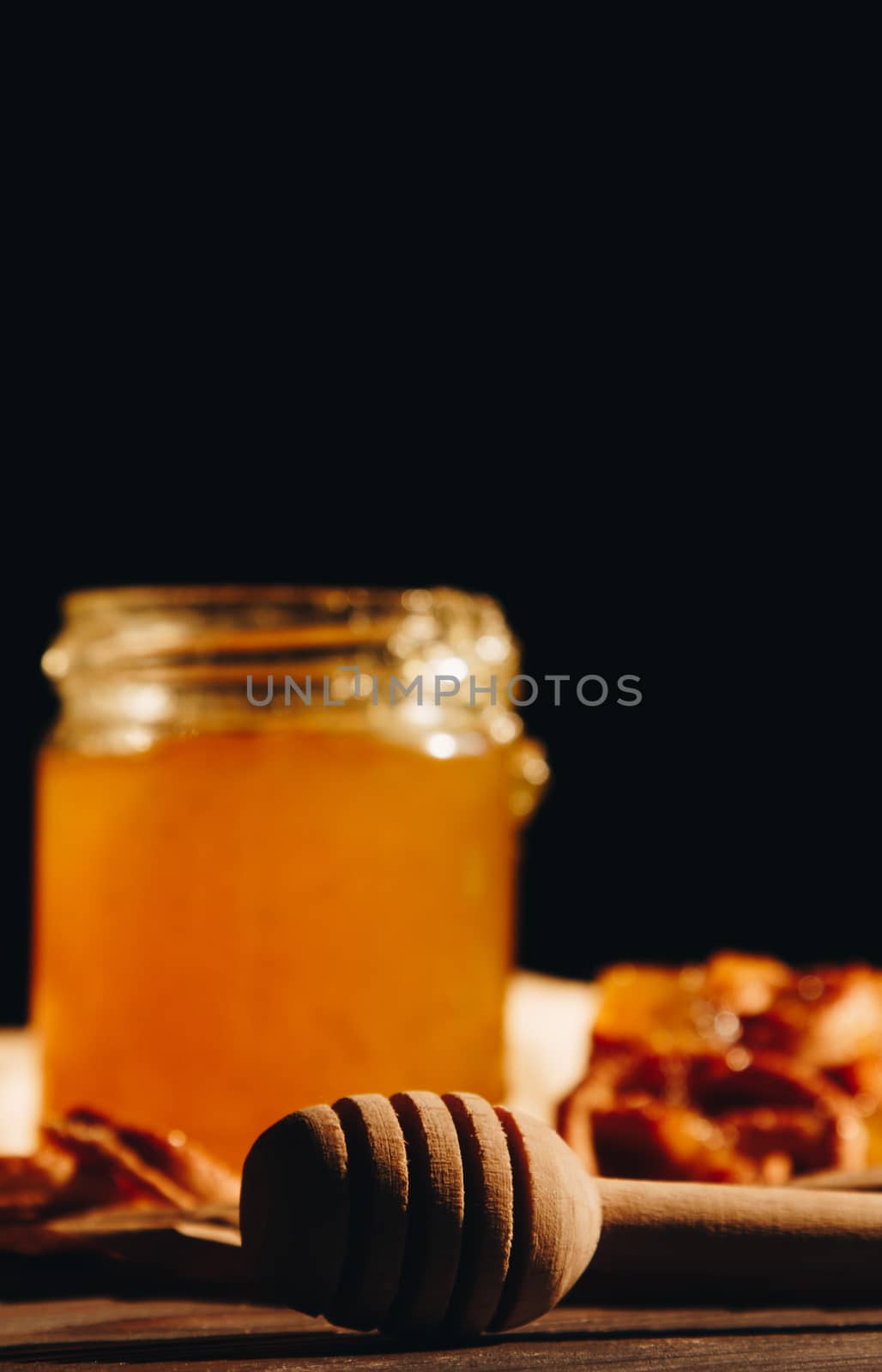 Honey with wooden honey dipper paper napkin and fruits on wooden table close up by yulaphotographer