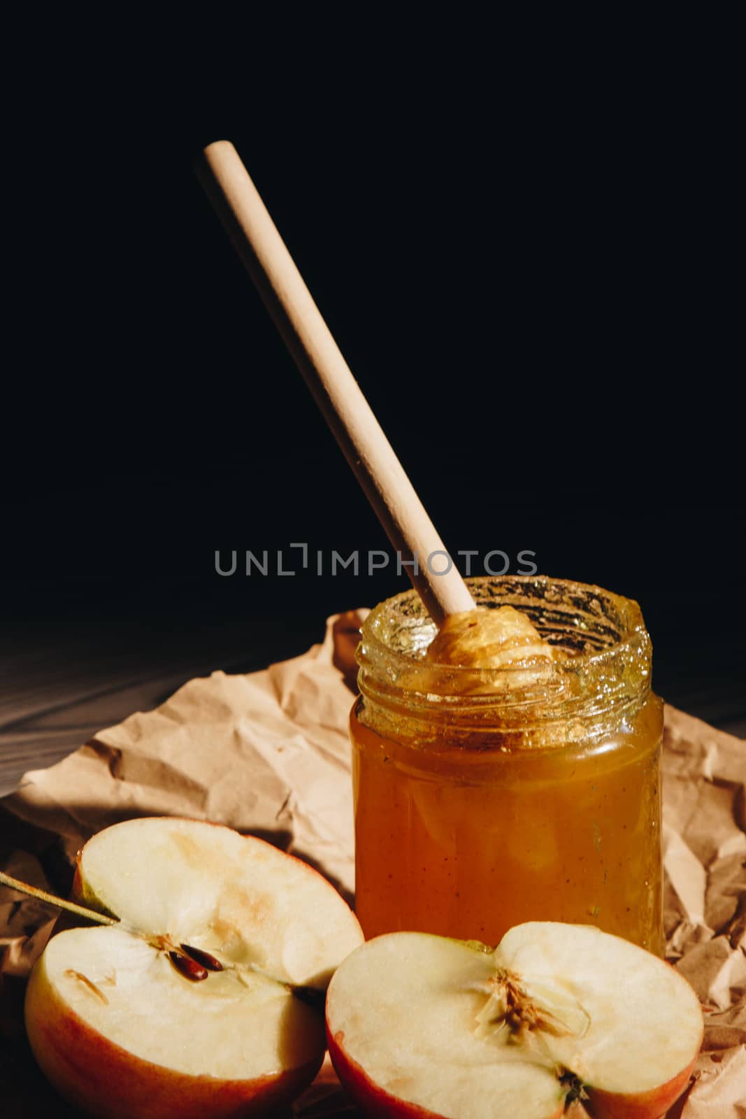 Honey with wooden honey dipper paper napkin and fruits on wooden table close up by yulaphotographer