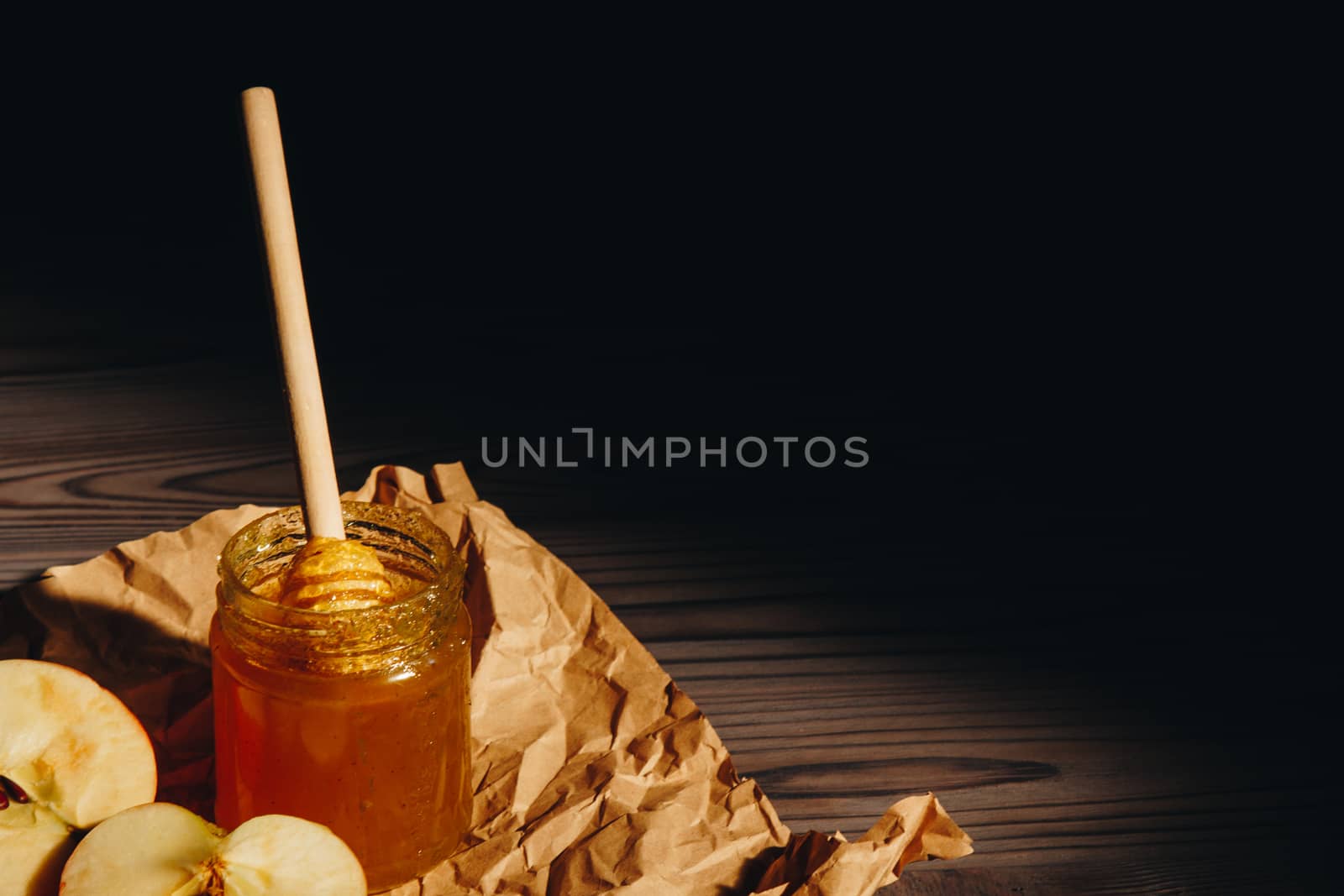 Honey with wooden honey dipper paper napkin and fruits on wooden table close up by yulaphotographer