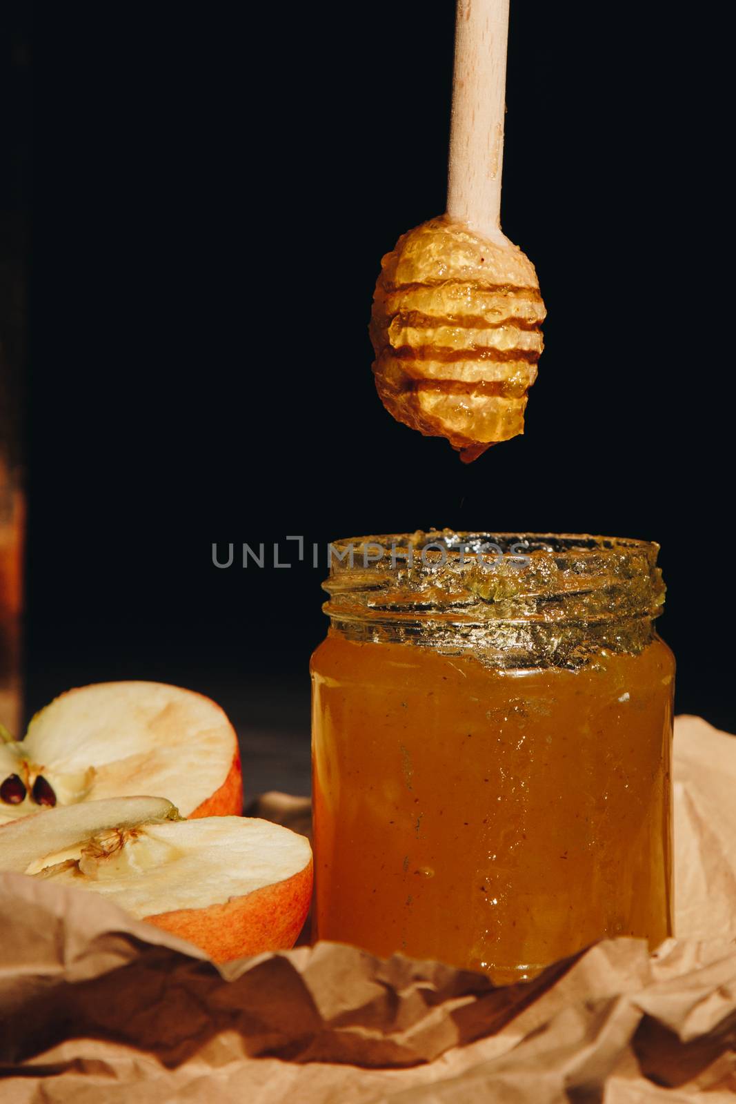 Honey with wooden honey dipper paper napkin and fruits on wooden table close up by yulaphotographer