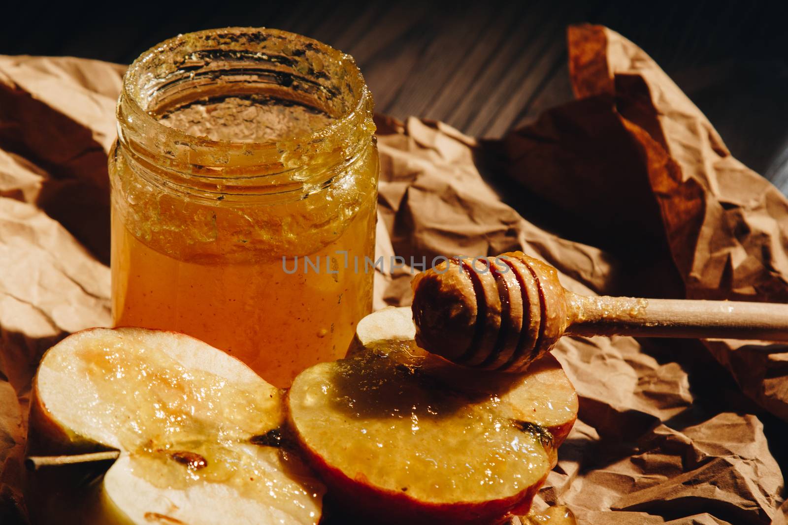 Honey with wooden honey dipper paper napkin and fruits on wooden table close up by yulaphotographer