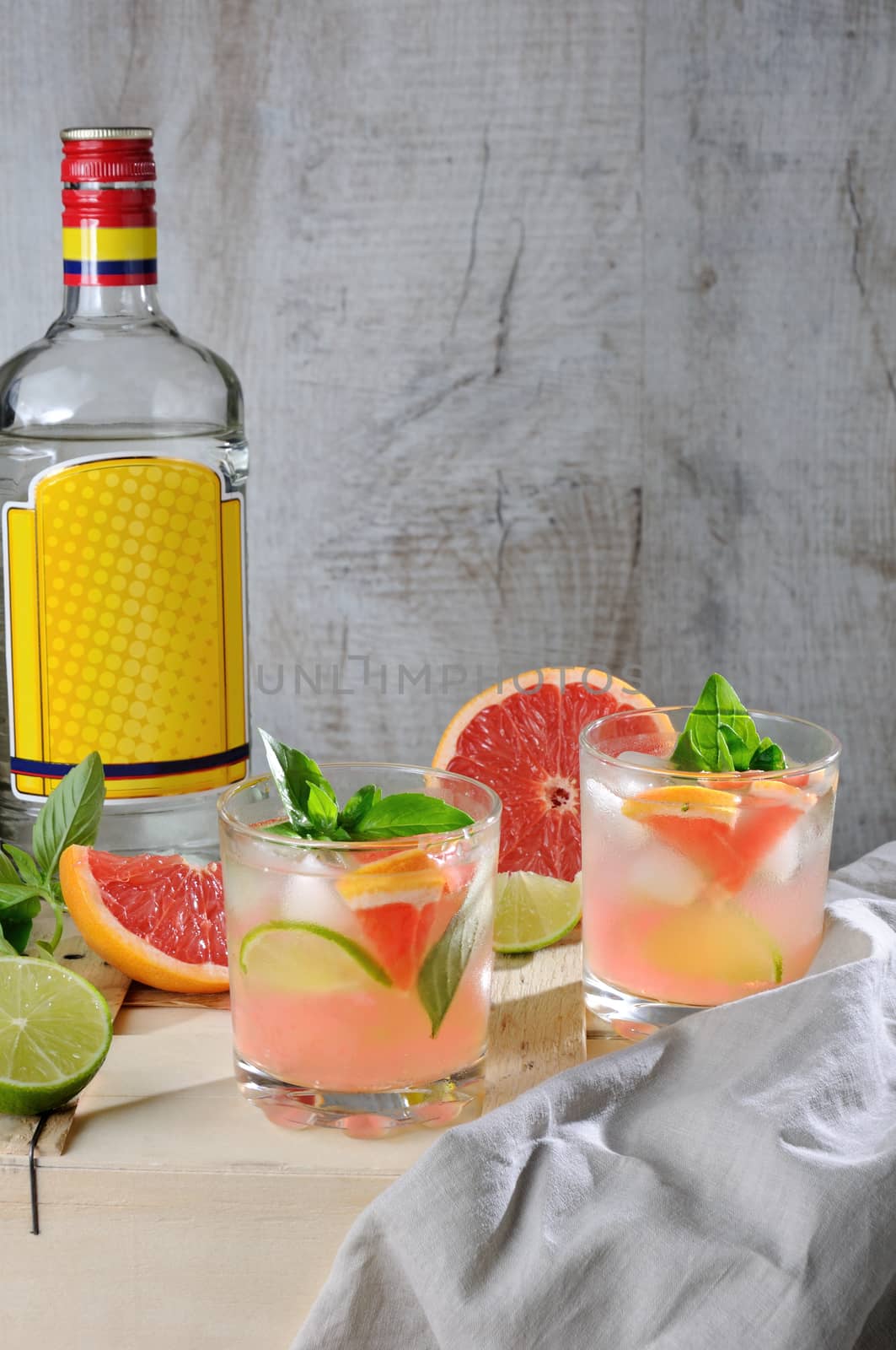 Cocktail from London dry gin with juice from squeezed red grapefruit and leaves of delicate basil of lemon, lime slices and chilled ice cubes.