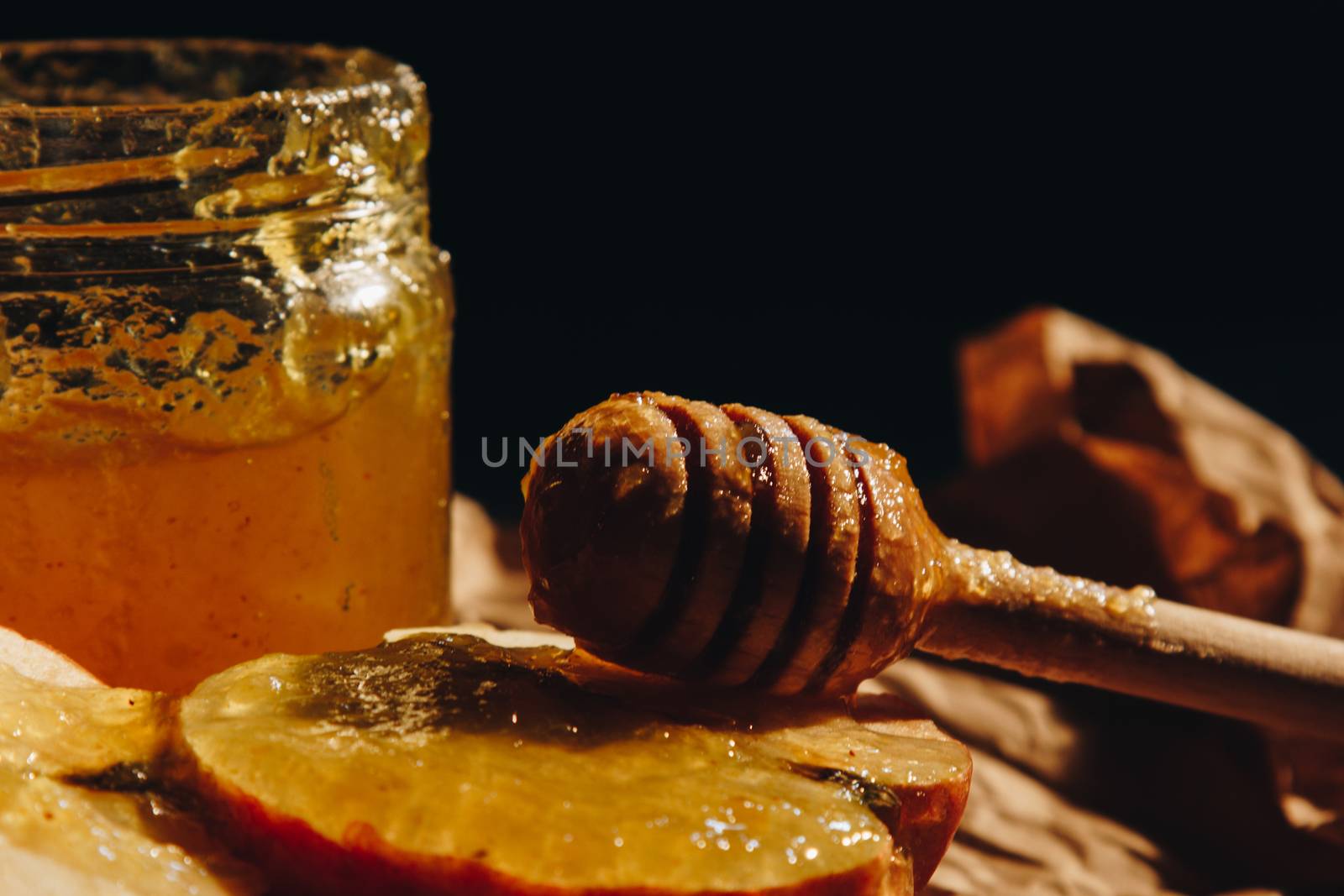 Honey with wooden honey dipper and fruits on wooden table close up