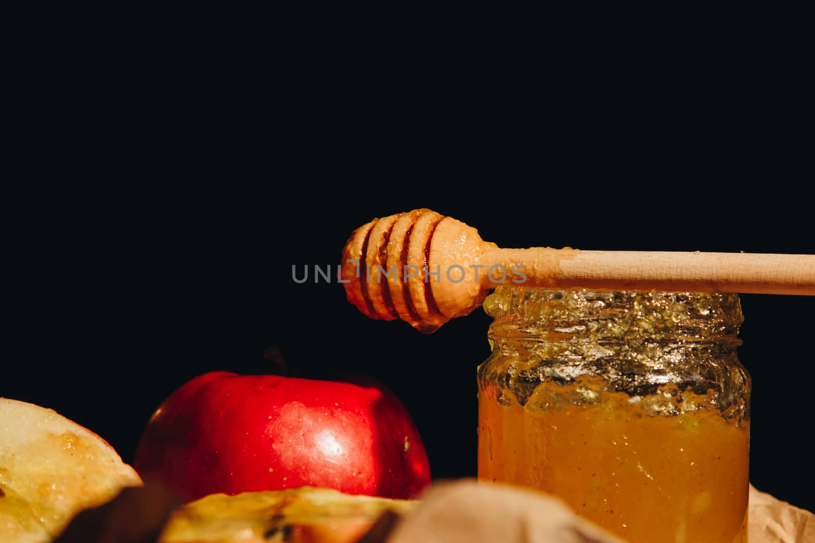 Honey with wooden honey dipper paper napkin and fruits on wooden table close up by yulaphotographer