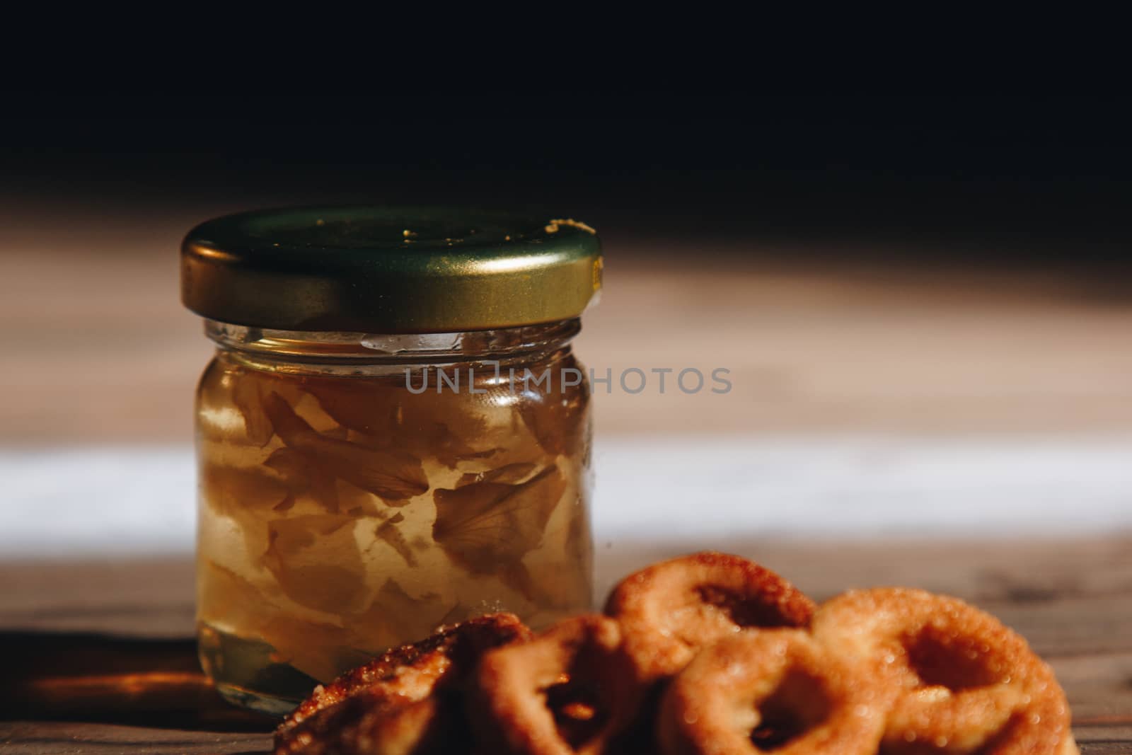 jar of honey with bagels on wooden table close up with honey dipper on black background