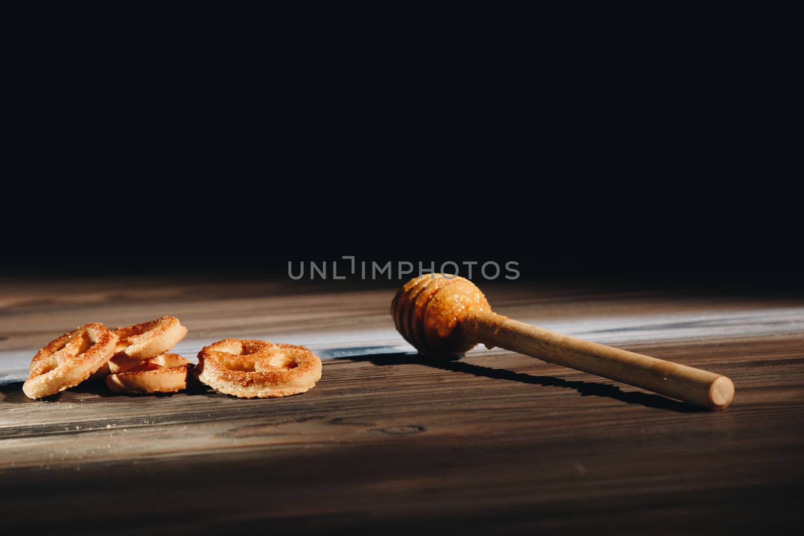 jar of honey with bagels on wooden table close up with honey dipper on black background