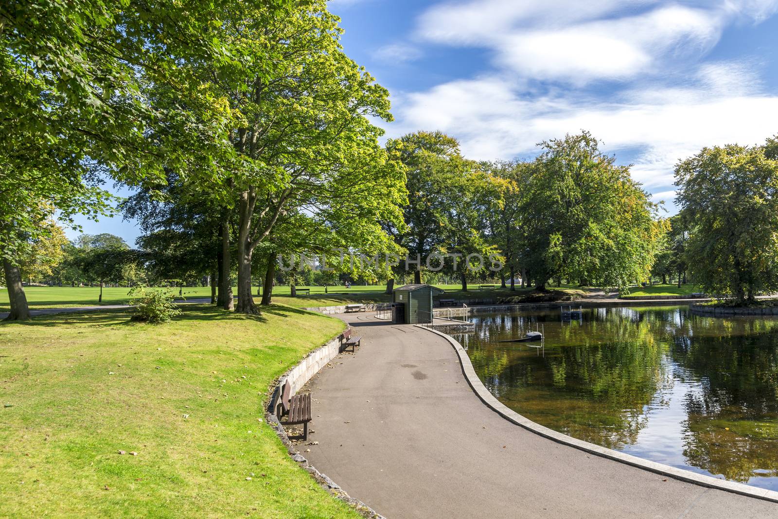 Scenic footpath with benches around a small shallow pond in Duthie park, Aberdeen, Scotland by anastasstyles