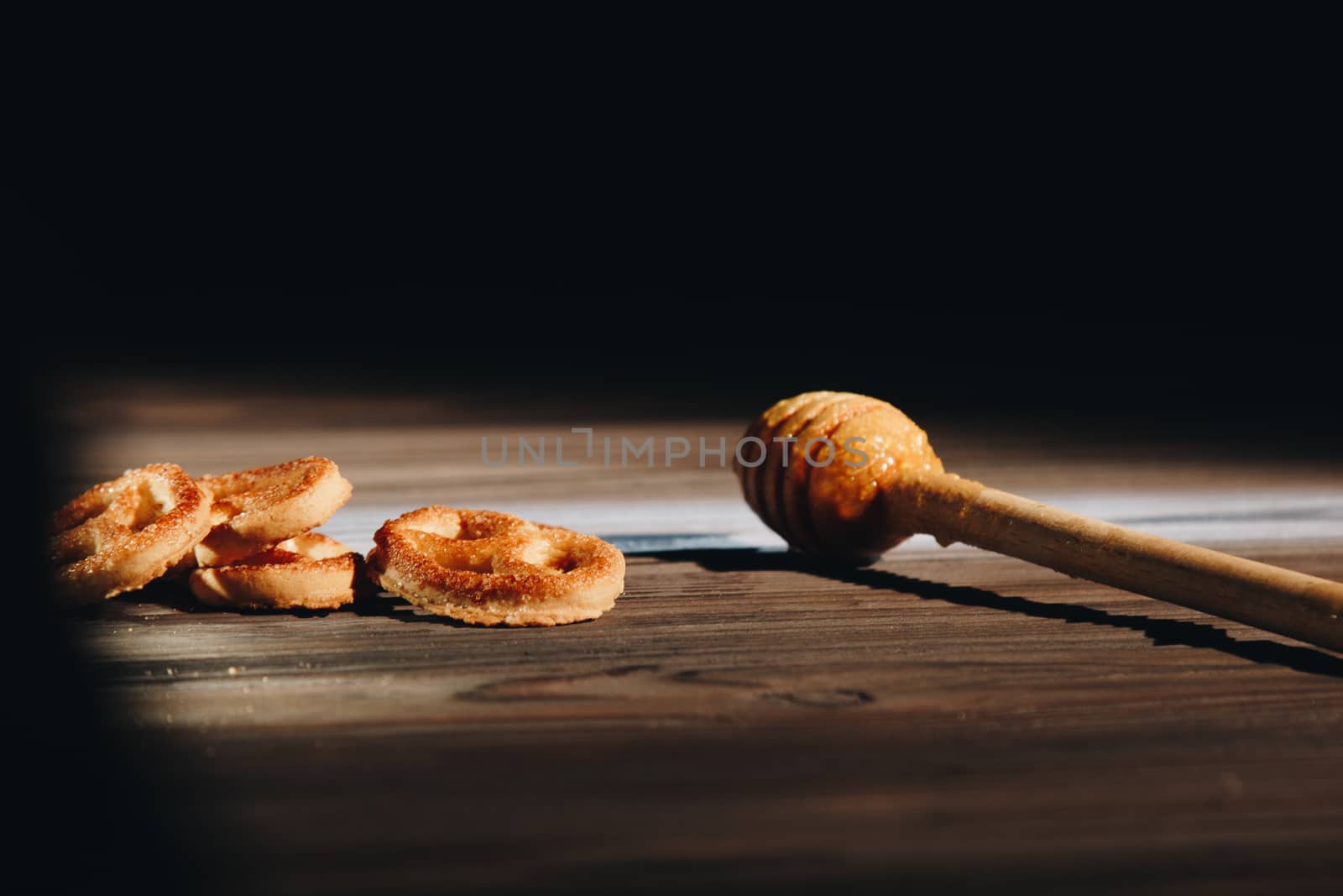 jar of honey with bagels on wooden table close up with honey dipper on black background