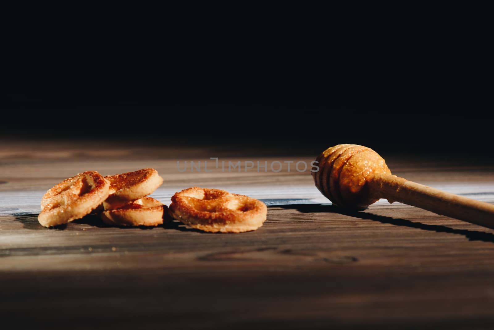 jar of honey with bagels on wooden table close up with honey dipper on black background