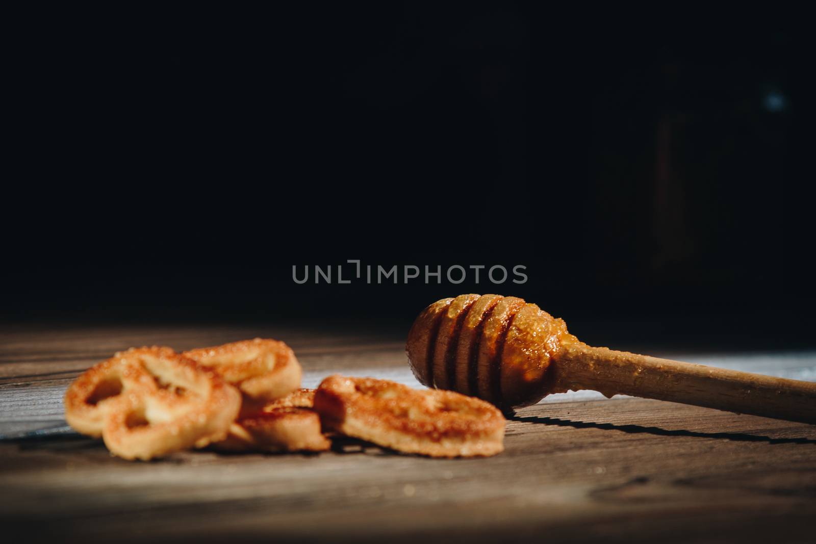 jar of honey with bagels on wooden table close up with honey dipper by yulaphotographer