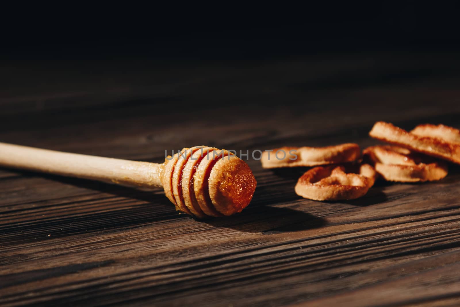 jar of honey with bagels on wooden table close up with honey dipper on black background