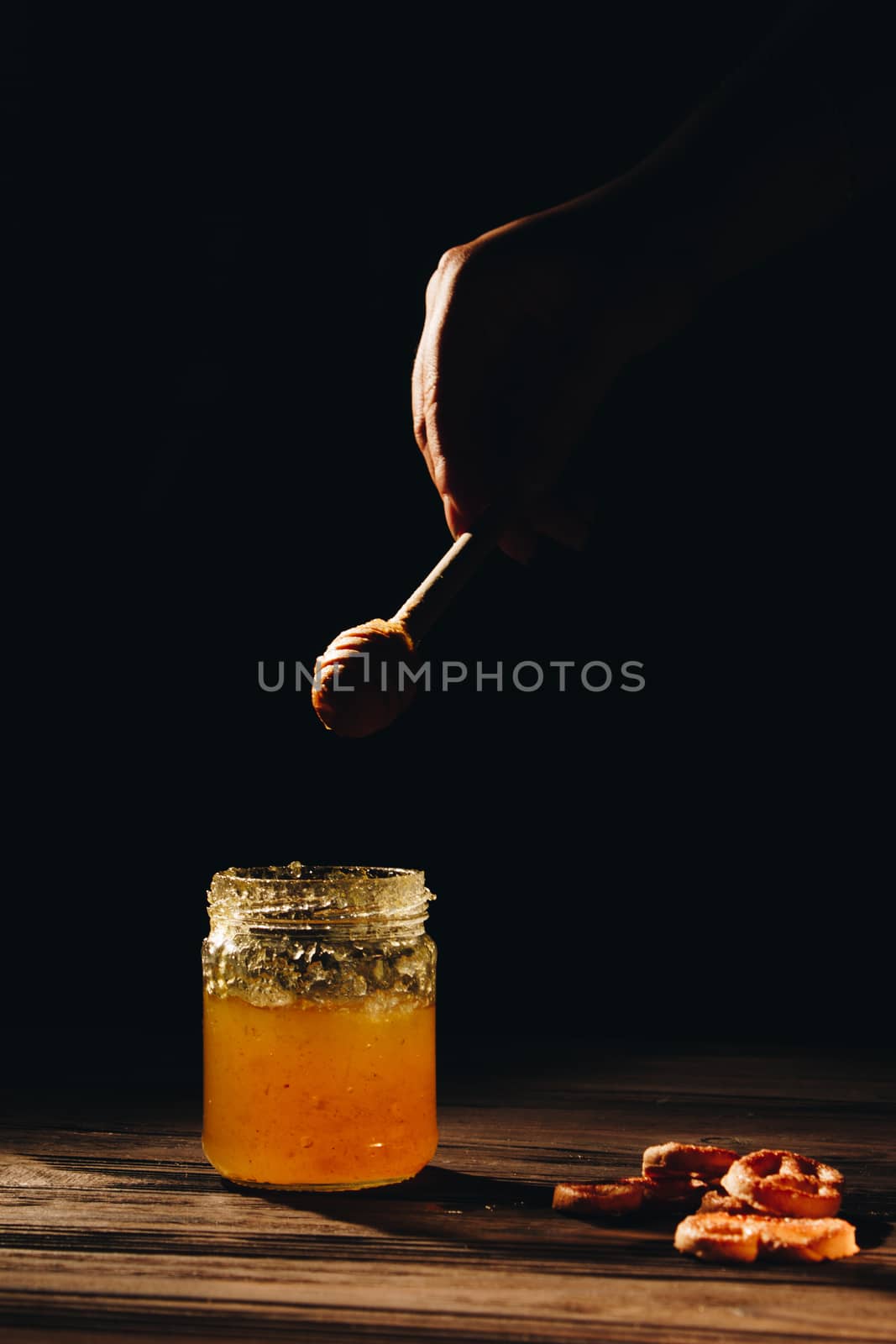 jar of honey with bagels on wooden table close up with honey dipper by yulaphotographer