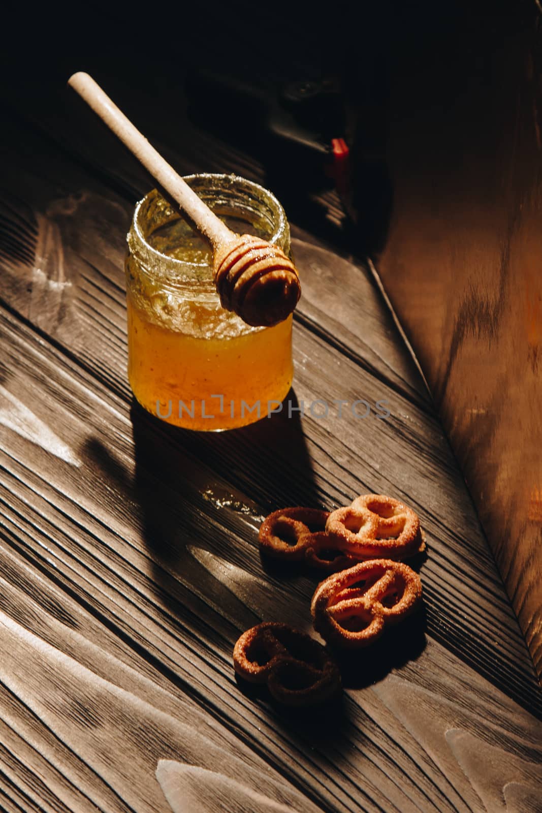 jar of honey with bagels on wooden table close up with honey dipper on black background