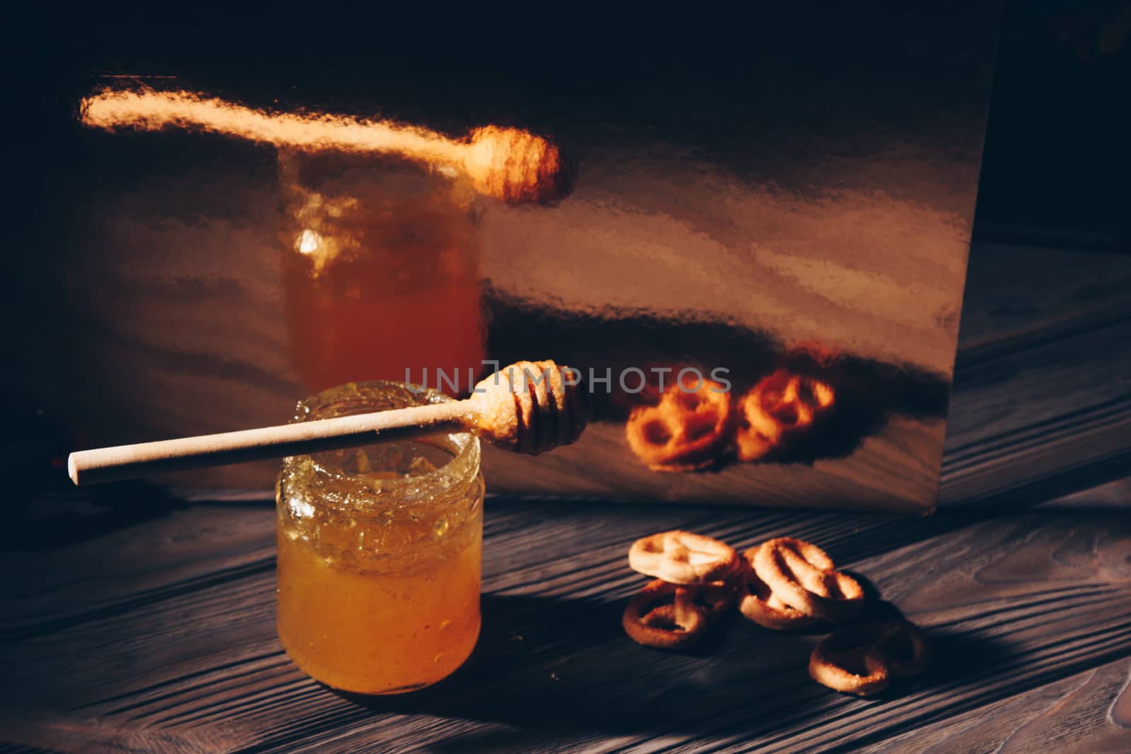 jar of honey with bagels on wooden table close up with honey dipper by yulaphotographer