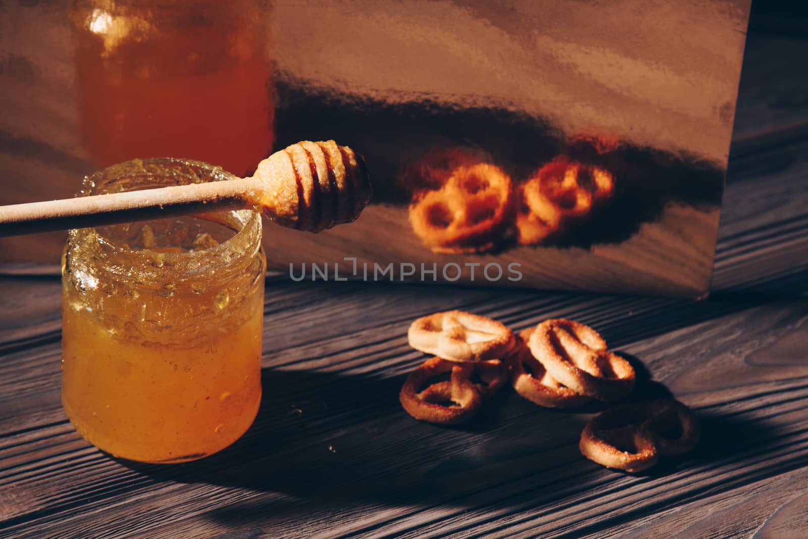 jar of honey with bagels on wooden table close up with honey dipper on black background