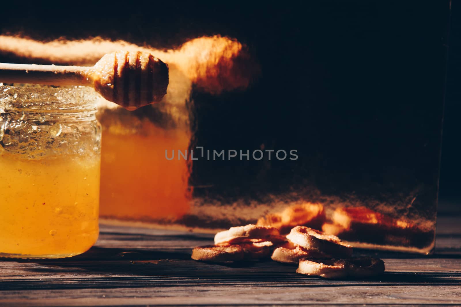 jar of honey with bagels on wooden table close up with honey dipper on black background