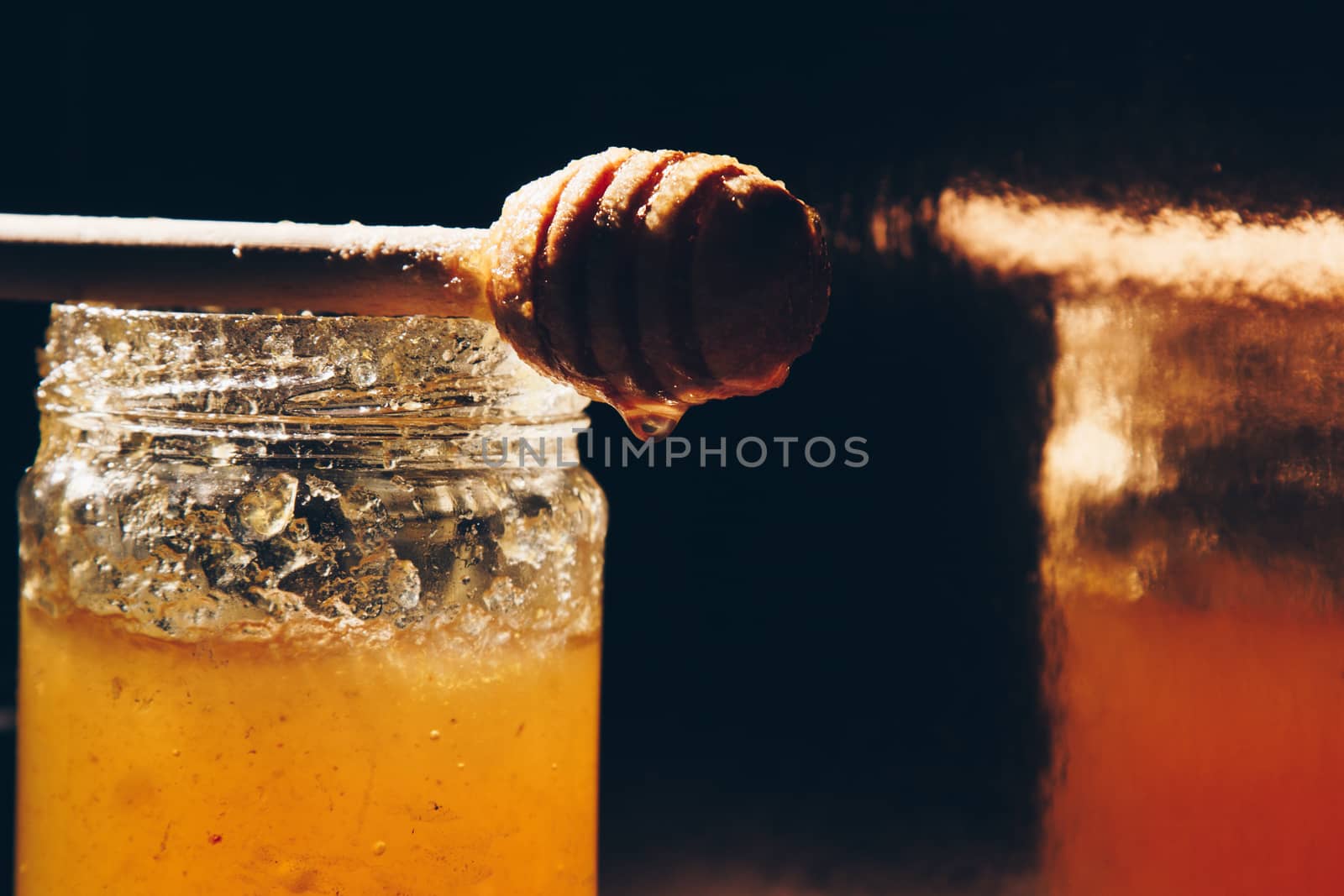 jar of honey with bagels on wooden table close up with honey dipper on black background