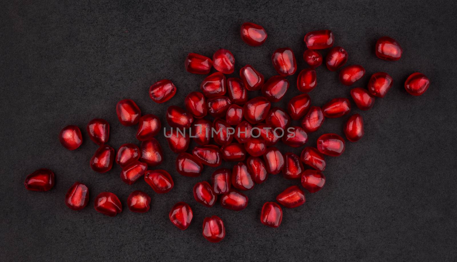 Pomegranate seeds on black background, top view, with empty space for text