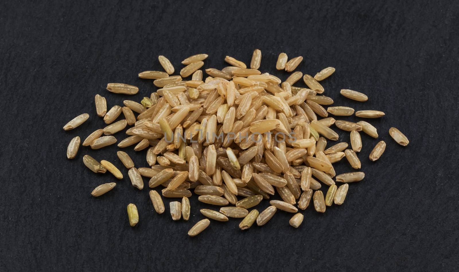 Heap of brown rice groats on black background