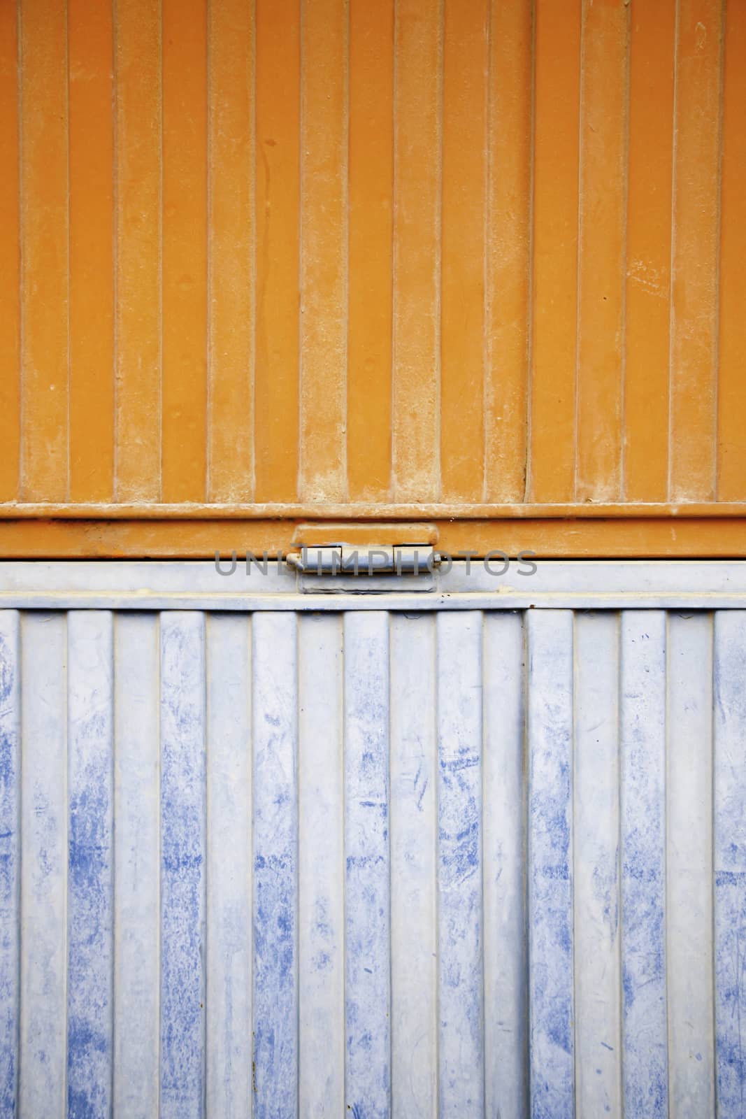 Wall decorated metal, detail of a closed metal door, painted in orange and blue