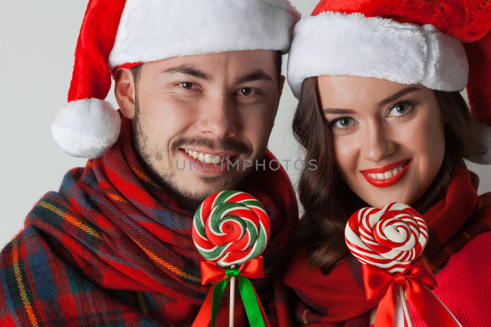 Young happy funny couple in christmas santa hats with lollipops