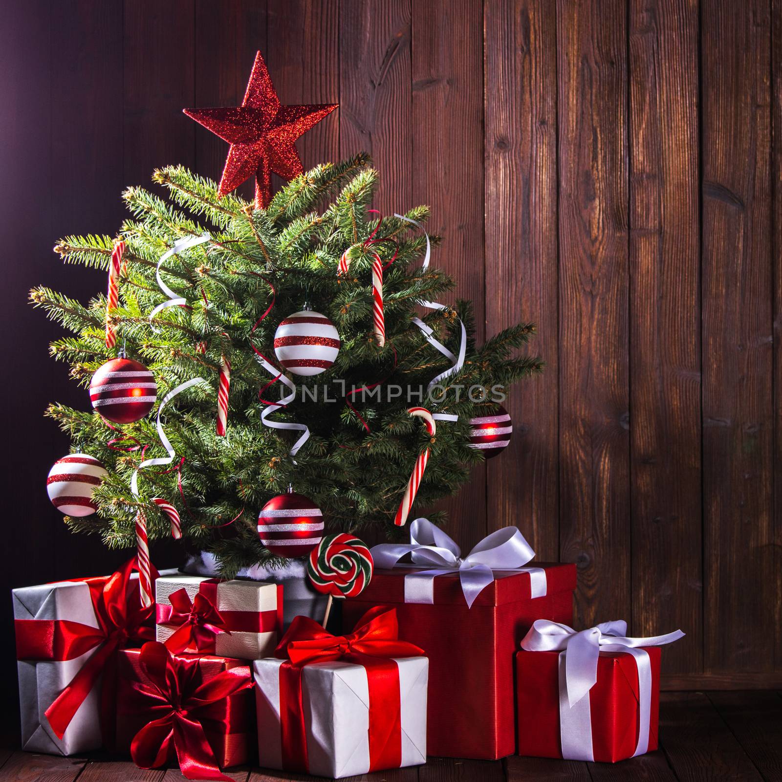 Decorated Christmas tree with candy canes , star , striped baubles and gift boxes on wooden background