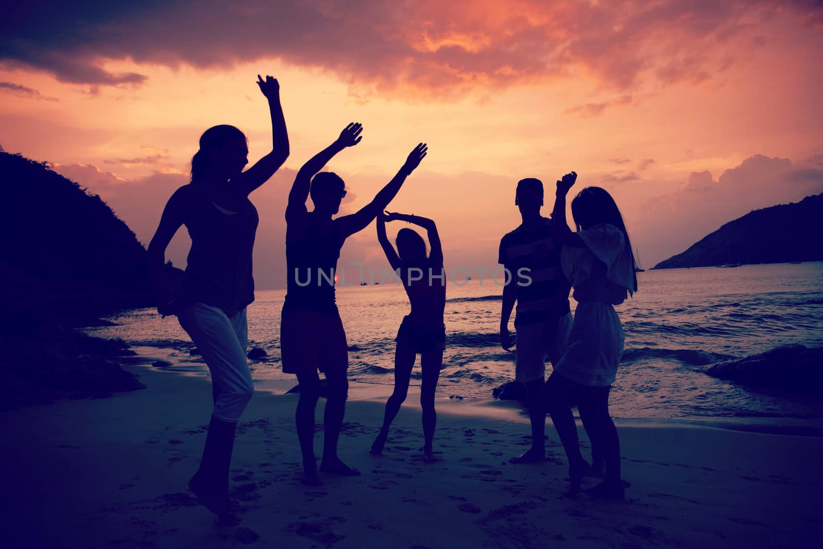 Group of happy people dancing at sea beach at sunset