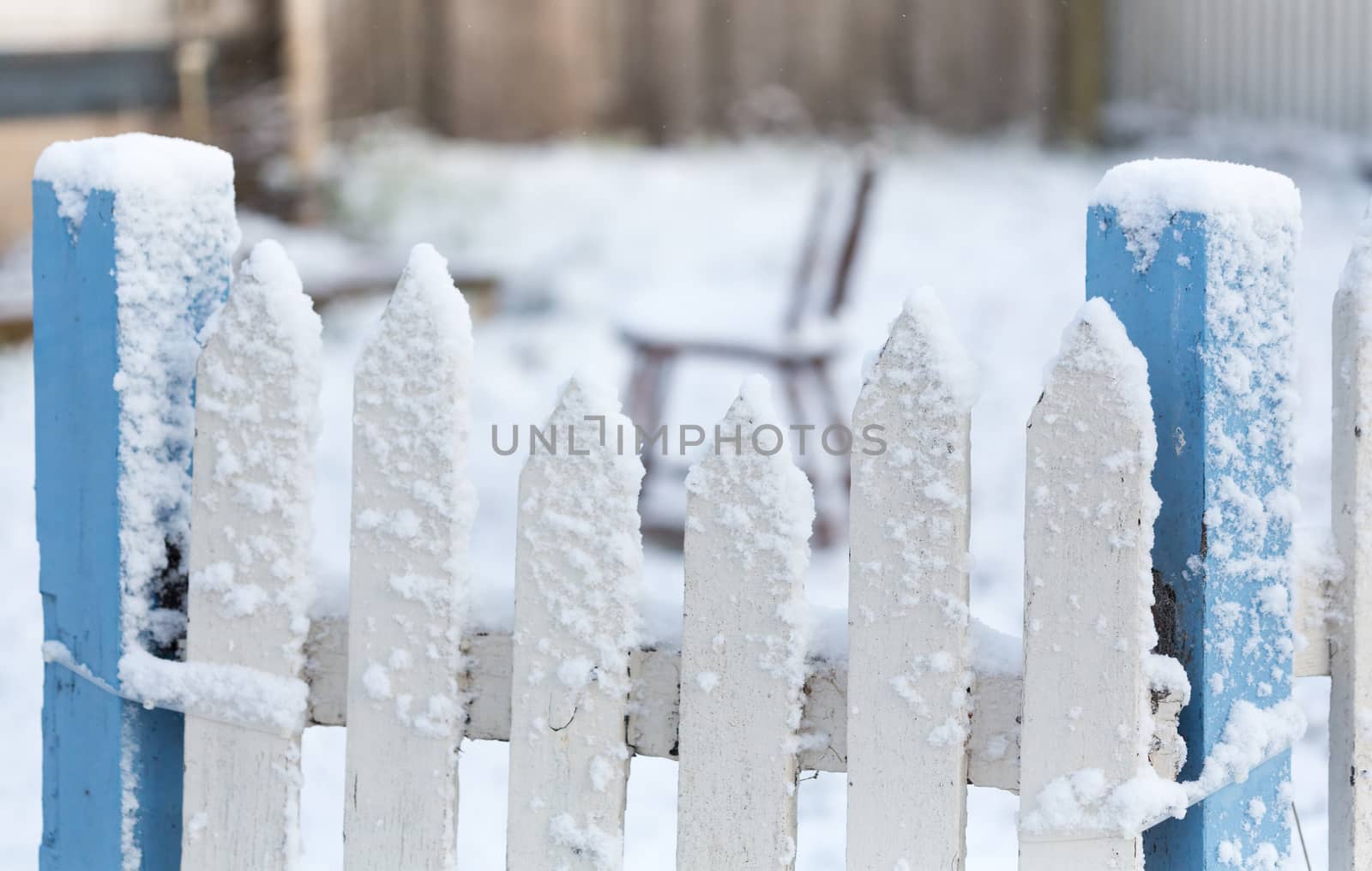 Snow covered white and blue picket fence with falling snow flakes in winter