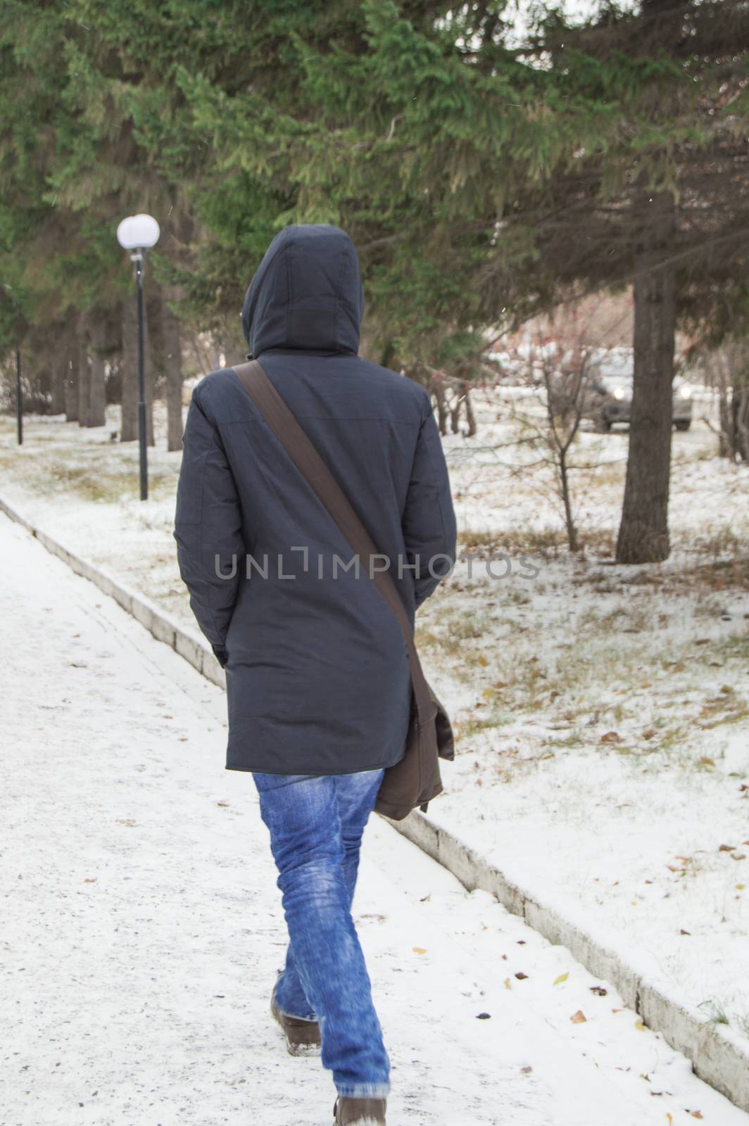 stylish hipster in a jacket with a hood is fast on a snowy road in winter Park by claire_lucia