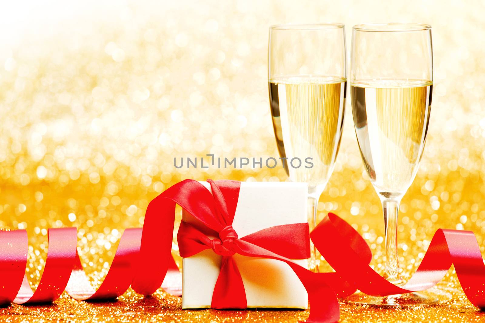 Champagne glasses and present in whitebox with red ribbon on golden background