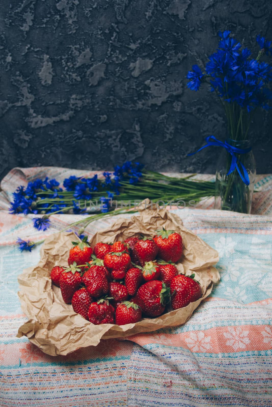 Seasonal summer flowers in vase blue cornflowers and fruits strawberries on a napkin close-up conceptual background