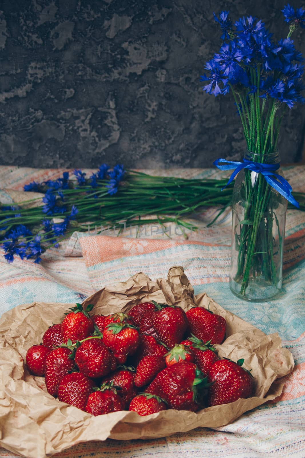 Seasonal summer flowers in vase blue cornflowers and fruits strawberries on a napkin close-up conceptual background