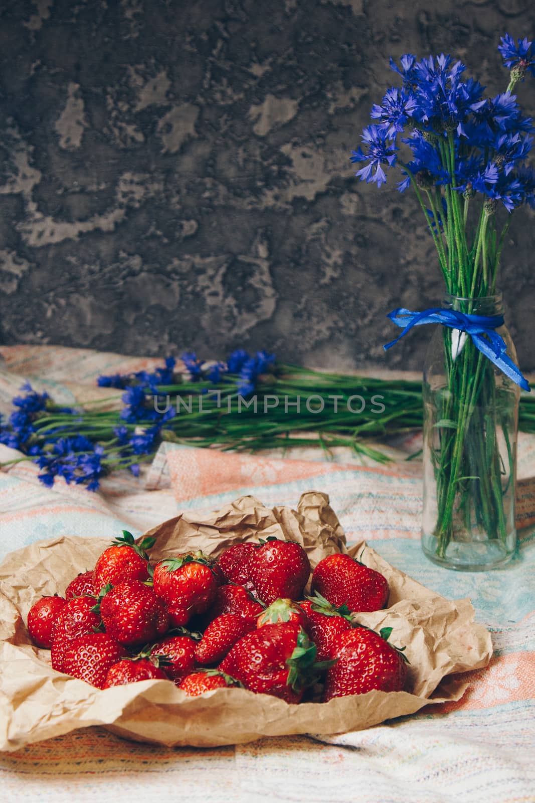 Seasonal summer flowers in vase blue cornflowers and fruits strawberries on a napkin close-up conceptual background