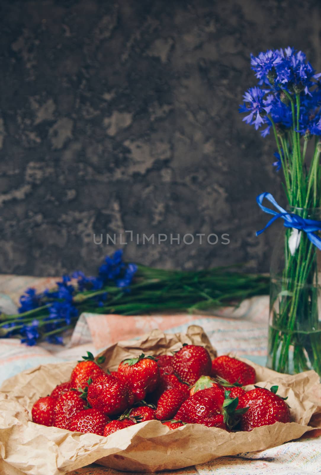Seasonal summer flowers in vase blue cornflowers and fruits strawberries on a napkin close-up conceptual background