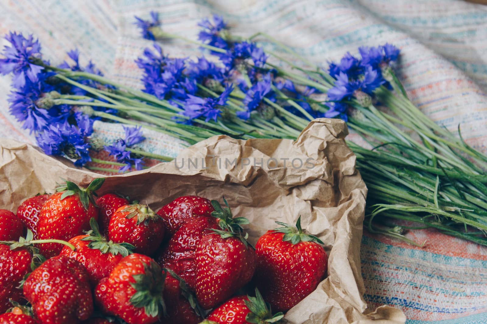 Seasonal summer flowers blue cornflowers and fruits strawberries on a napkin close-up conceptual background by yulaphotographer