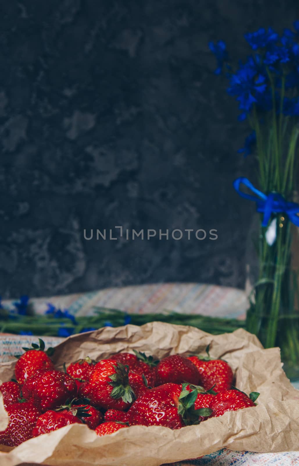 Seasonal summer flowers in vase blue cornflowers and fruits strawberries on a napkin close-up conceptual background