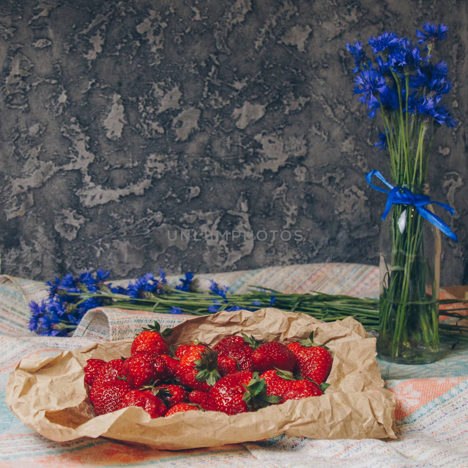 Seasonal summer flowers in vase blue cornflowers and fruits strawberries on a napkin close-up conceptual background