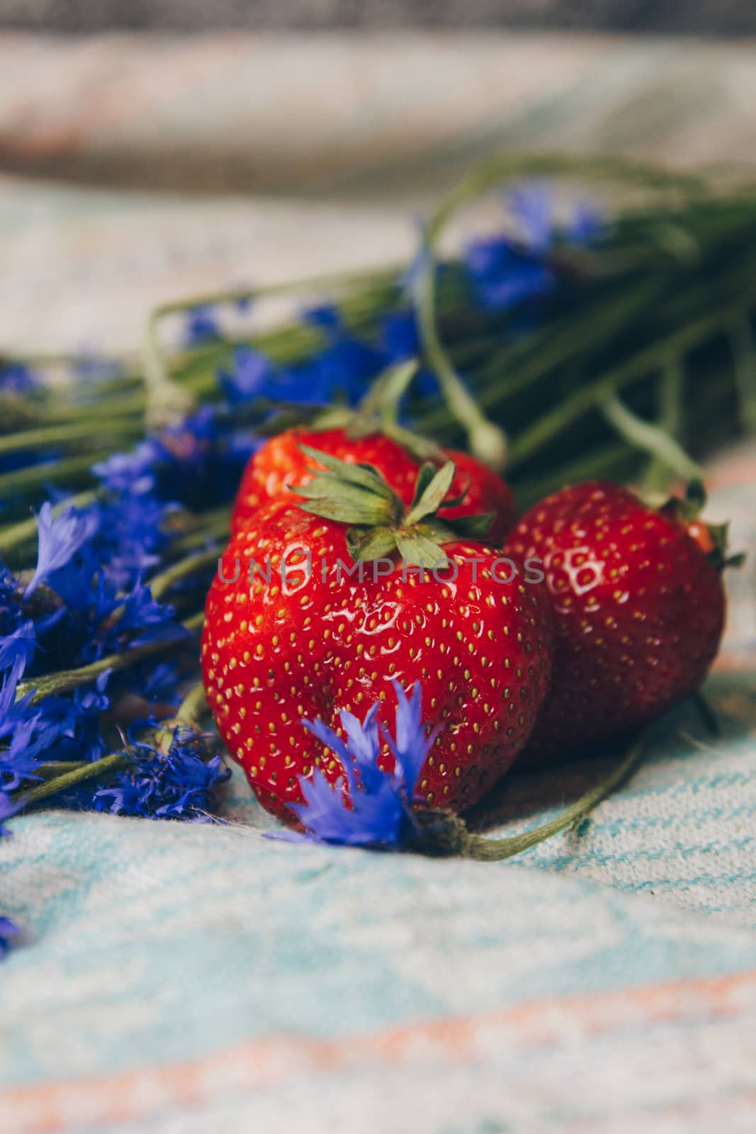 Seasonal summer flowers in vase blue cornflowers and fruits strawberries on a napkin close-up conceptual background