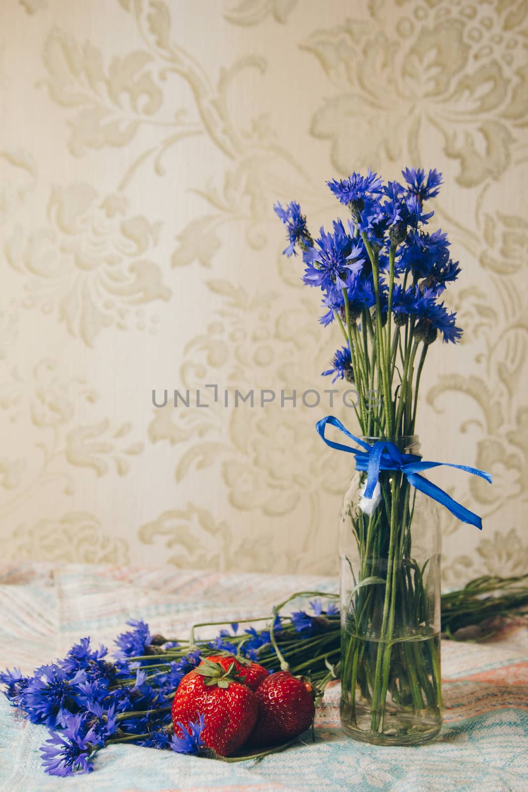 Seasonal summer flowers in vase blue cornflowers and fruits strawberries on a napkin close-up conceptual background