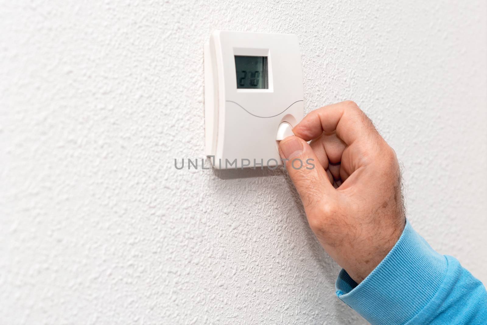 Man hand adjusting thermostat at home. Celsius temperature scale. by HERRAEZ